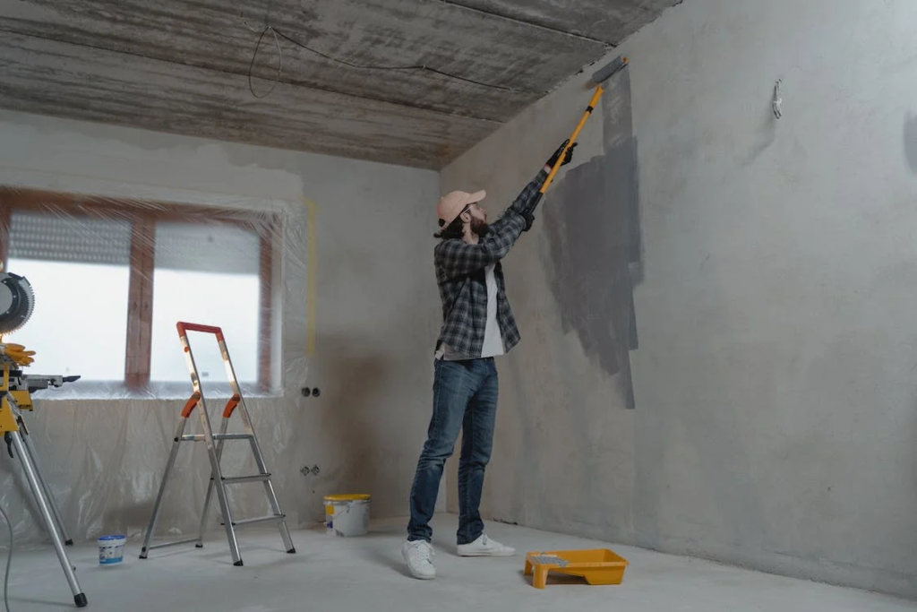 A photo showing a man painting a wall with a roller.