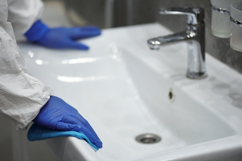 A photo showing a person with blue rubber gloves cleaning a sink