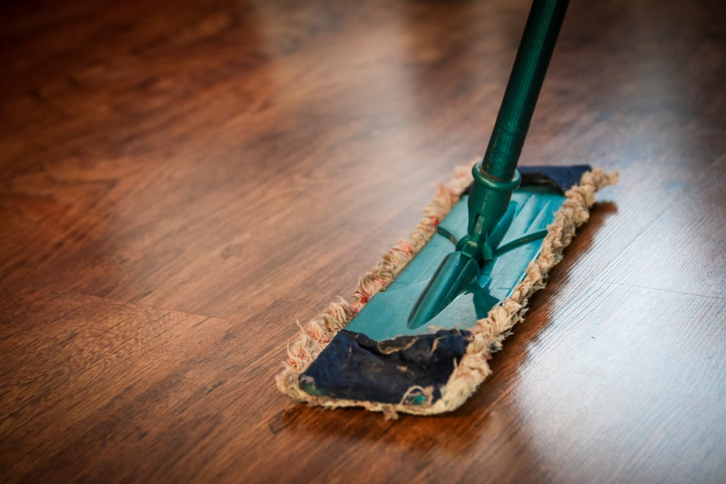 A photo showing a green mop resting on a wood floor