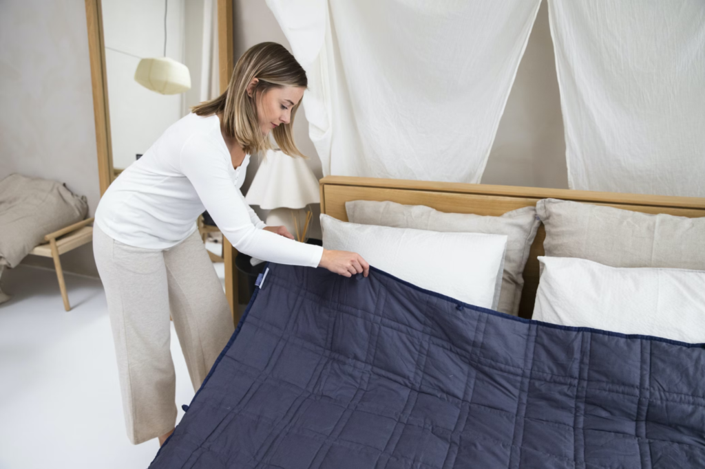 A photo showing a woman laying a blanket on a bed.